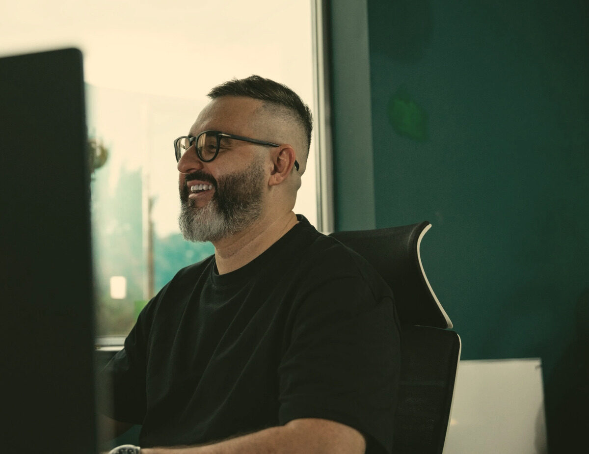 Tom Cheddadi laughing at his desk in the office, facing his monitor.
