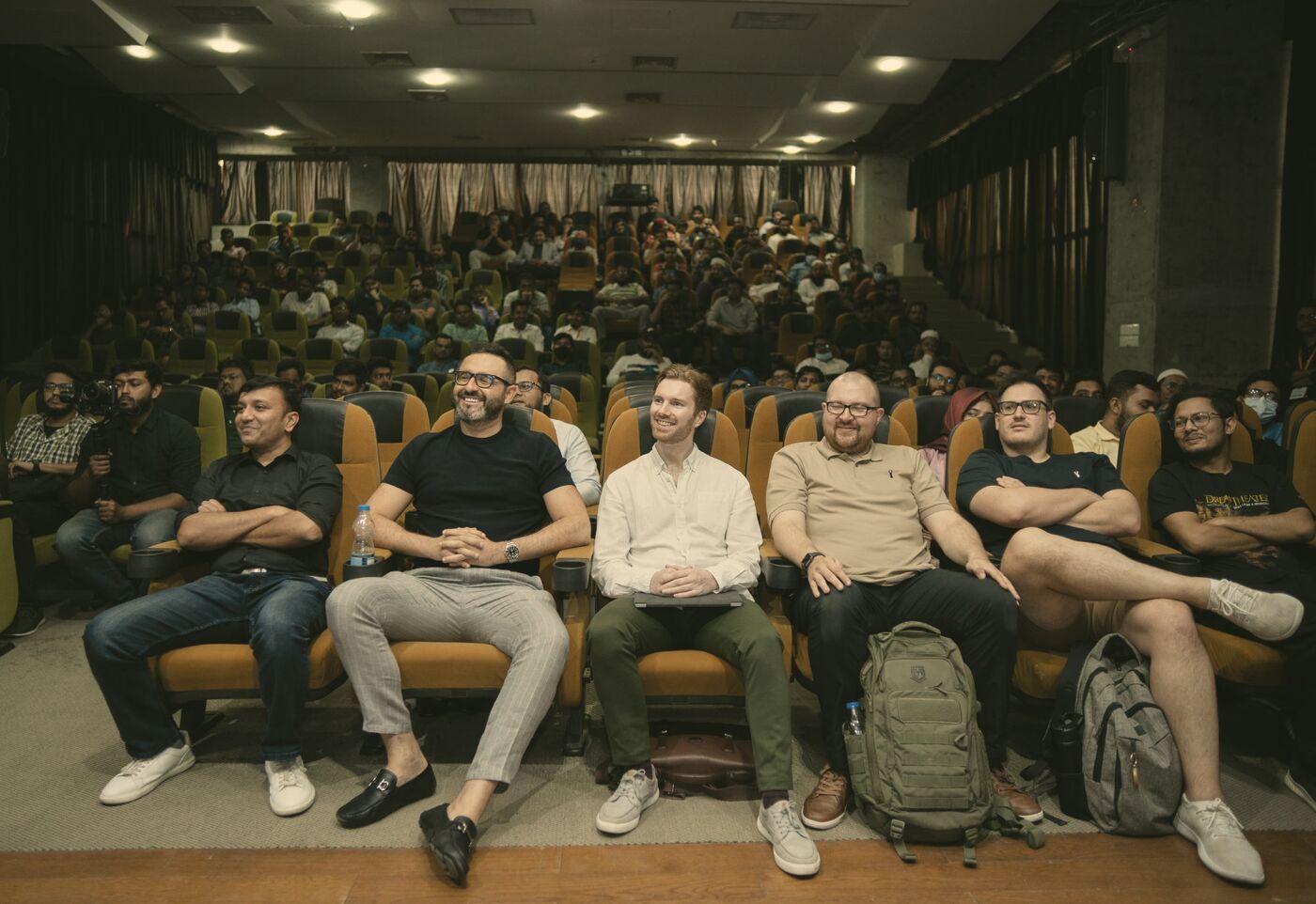 Tom smiling in the front row of a packed auditorium in Dhaka, beside four members of his leadership team.