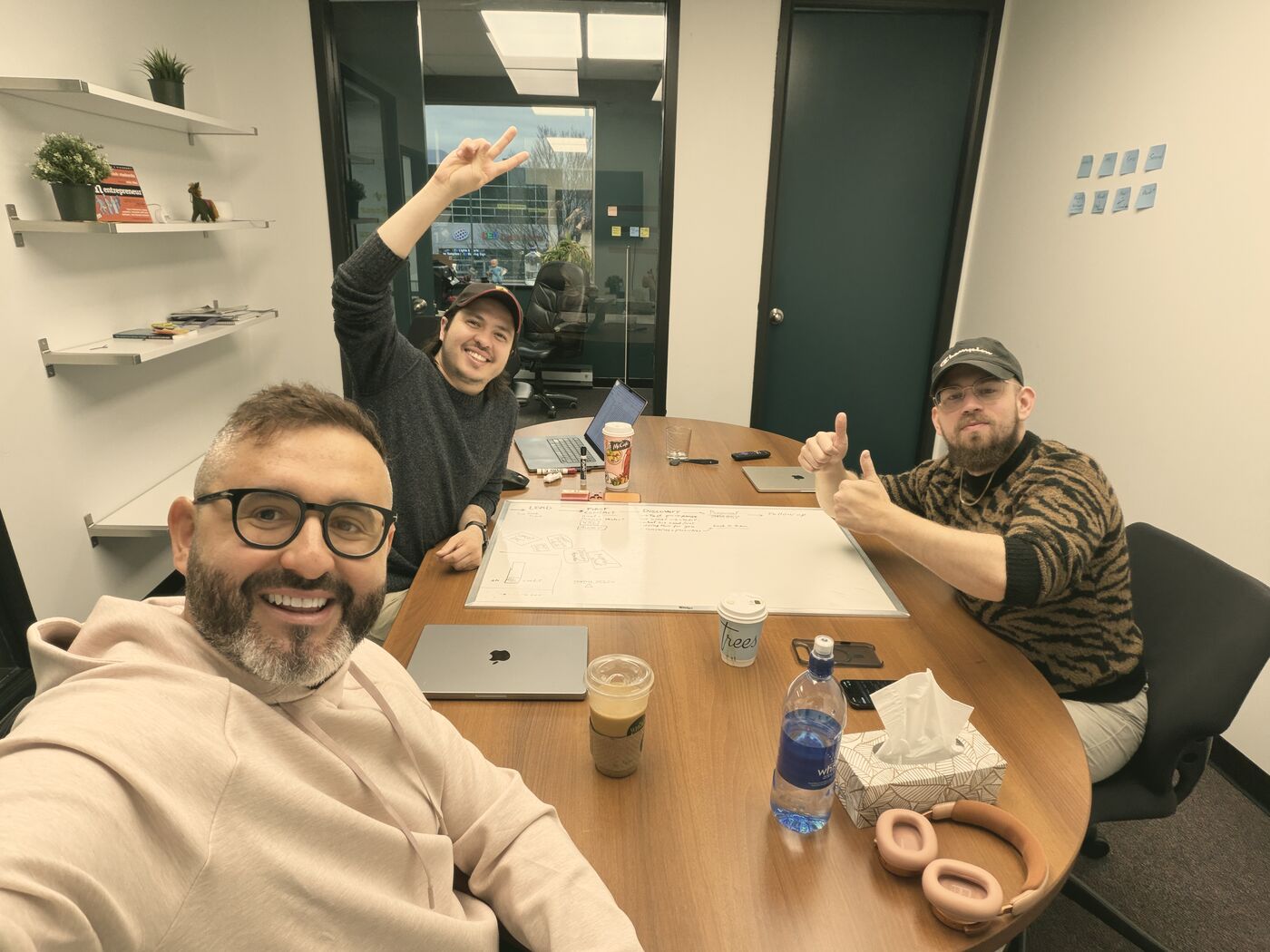 Tom taking a selfie at a meeting table with two Setsail teammates giving a thumbs up and a wave.