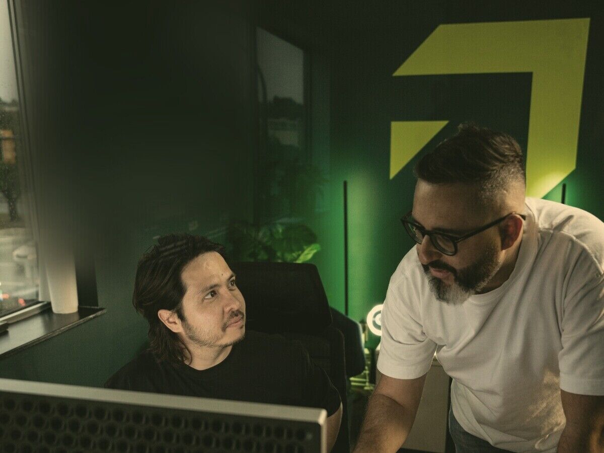 Tom leaning over a desk talking with Jason, the green Setsail mark on the wall behind them.